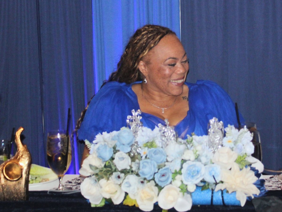 Lynette at her birthday celebration, surrounded by blue and white floral arrangements